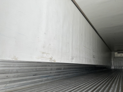 Trailer interior showing corrugated metal floor and sidewalls with faint marks and a small white unit at far end.