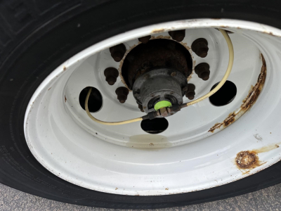 Wheel with white rim and tire showing a central hub and yellow electrical line; rust spots on rim and green cap visible near hub.
