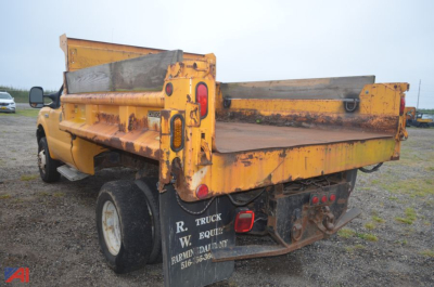 Ford F-350 dump truck bed with yellow paint and hydraulic dump mechanism, rear view showing tailgate and license area.