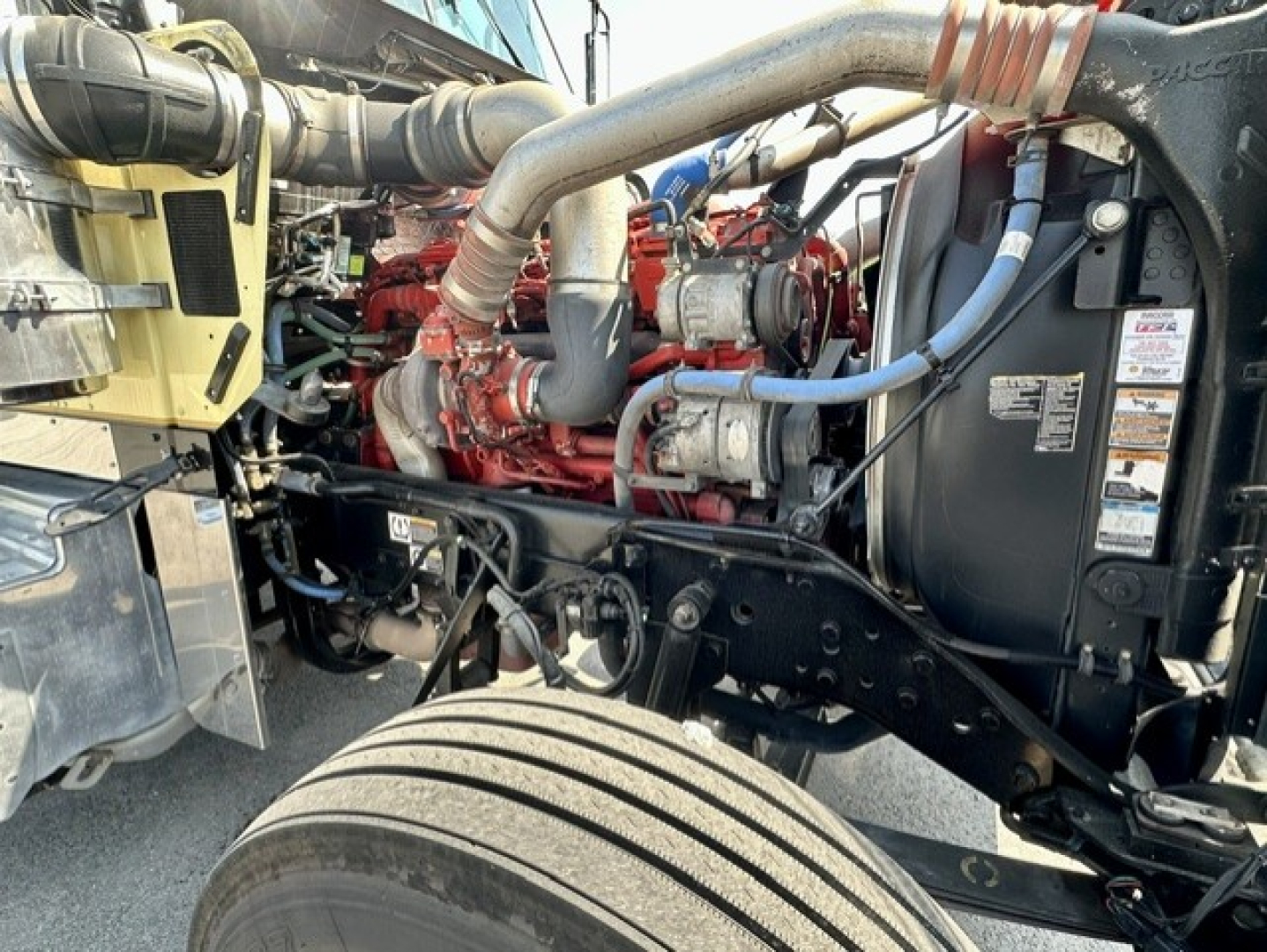 Kenworth W900L engine bay showing large cooling system hoses, red engine block, and black frame with wheel in foreground.