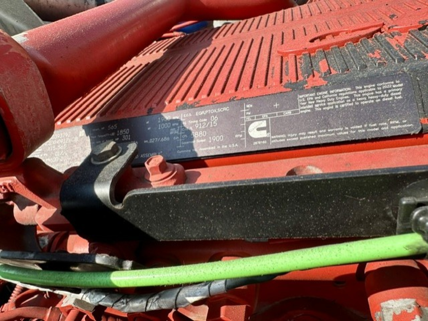 Kenworth W900L engine bay with label plate and green hose visible.
