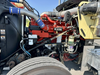 Kenworth W900L engine bay showing red inline ISX15 diesel engine and surrounding hoses and components.