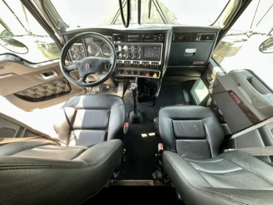 Kenworth W900L interior view showing steering wheel, dashboard with gauges, control switches, two captain chairs, and gear shifter.
