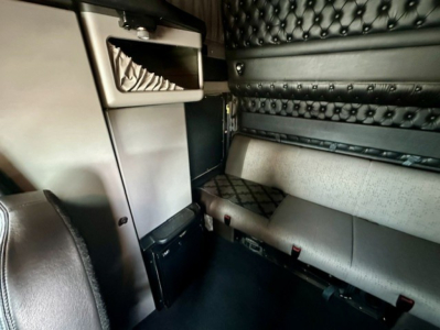 Kenworth W900L interior view showing sleeper area with black quilted headliner, storage cabinet, and seating along the wall.