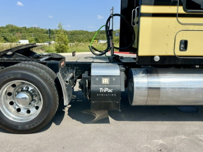 Kenworth W900L side view showing TriPac Evolution battery/equipment box mounted under cab and polished fuel tank with wheel and frame rail.