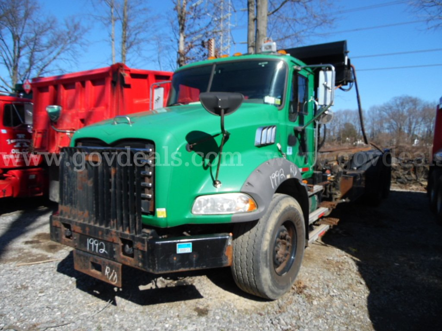Green 2008 Mack GU813 roll-off truck profile with front bumper guard and attached container, VIN 1M2AX18C38M001339 visible on cab; stock number 32136-71; truck in service.