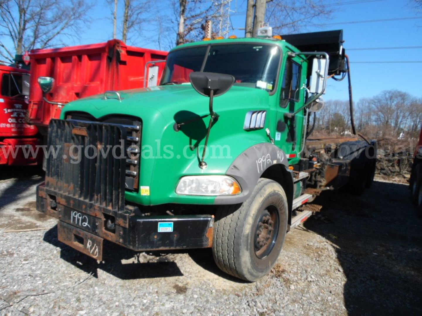 Green Mack GU813 roll-off truck front view showing large black grille guard and side mirrors.