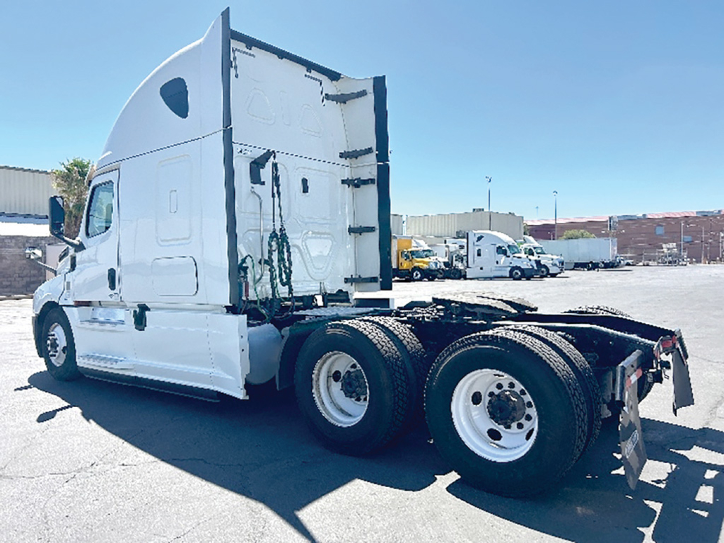Freightliner Cascadia126 sleeper truck side rear showing drivetrain and dual rear axles with white paint and trailer hitch.