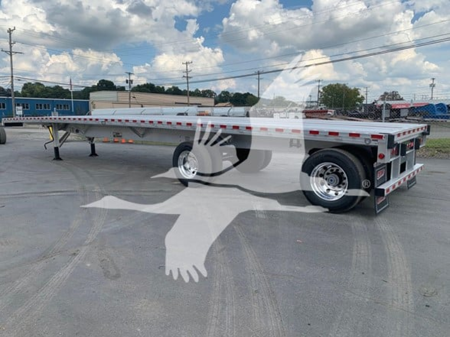 CK-100 flatbed trailer by Reitnouer showing long deck and dual rear axles with reflective tape and metal stake pockets.