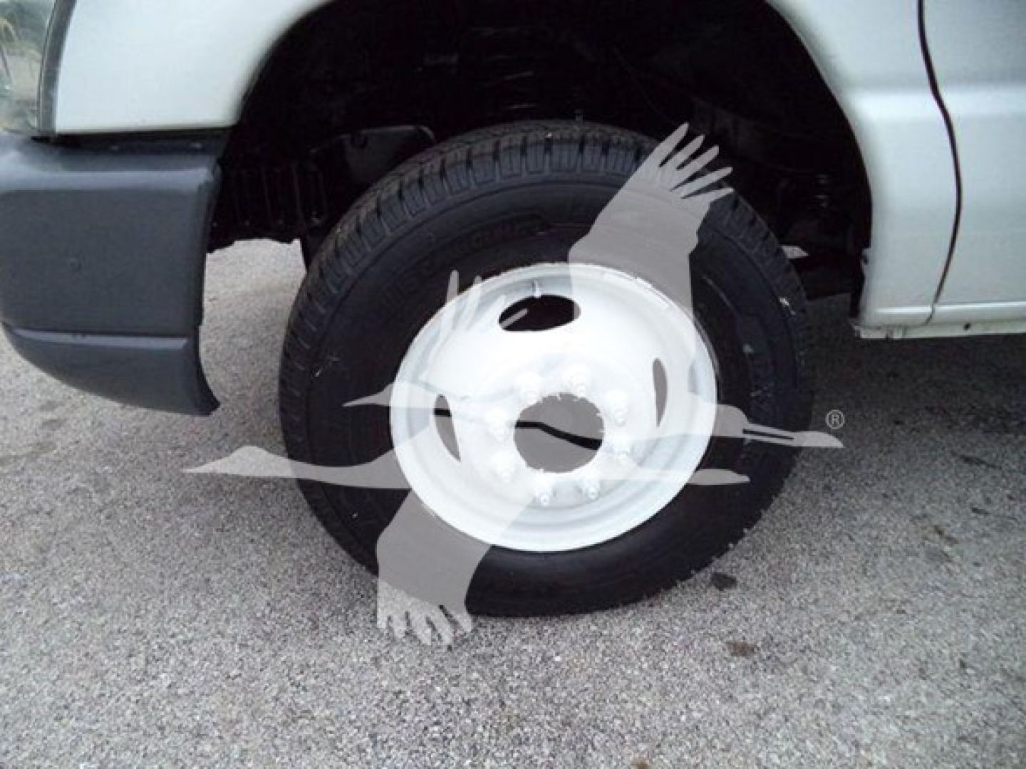 Ford E-Series van front wheel well and tire with white steel wheel visible in side view.