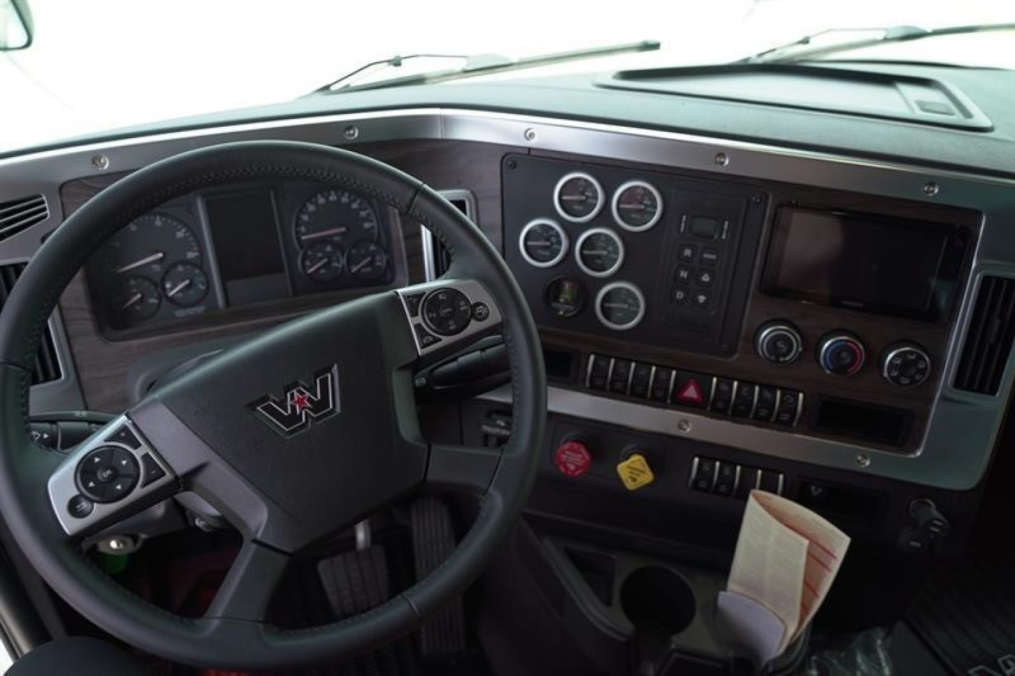 Dashboard and steering wheel view inside a Western Star 47X truck cab showing gauges, controls, and a spill of papers.