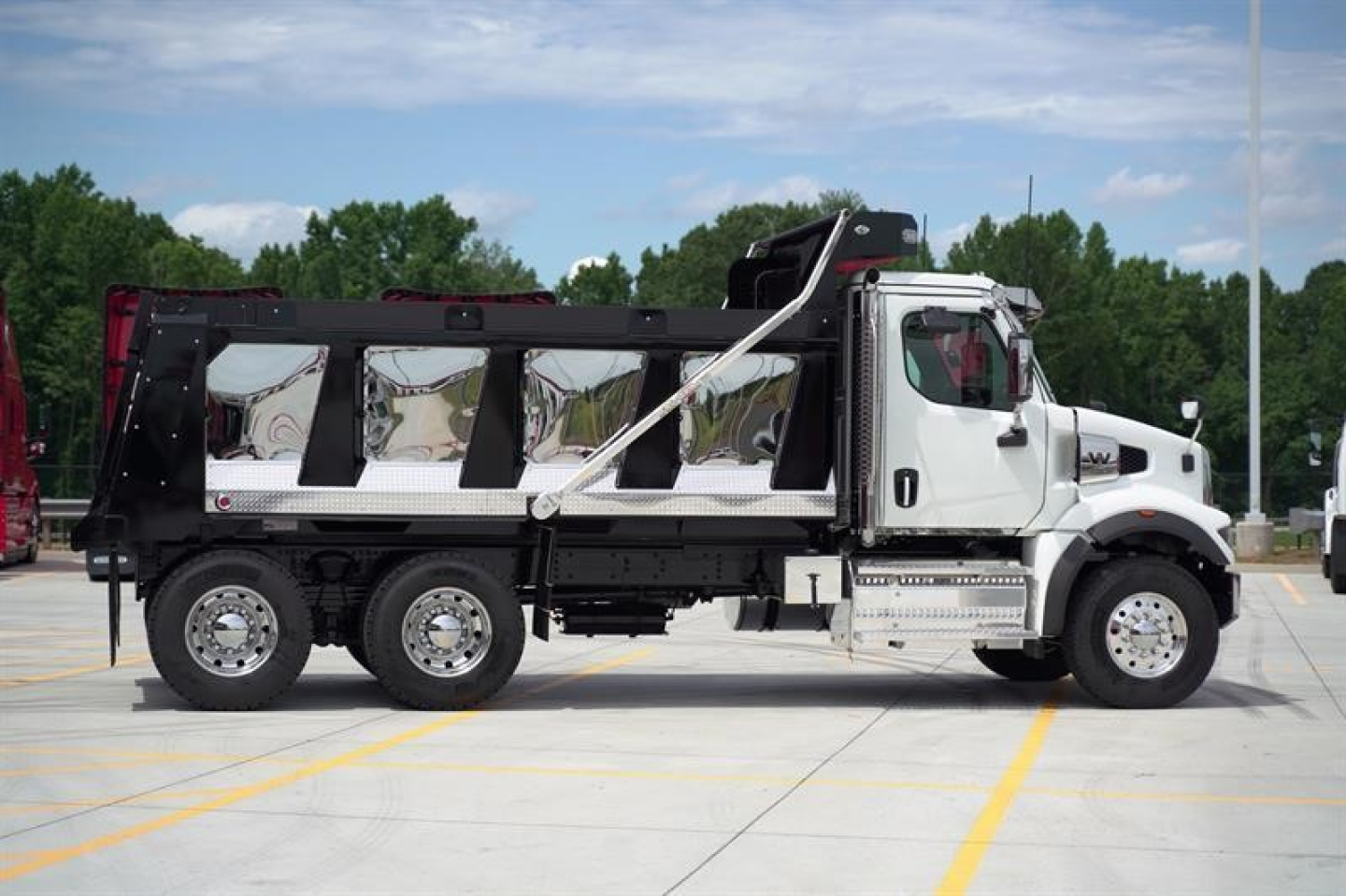 Western Star 47X dump truck side view showing white cab and black dump body with hydraulic lift, three-axle configuration, in a parking lot.