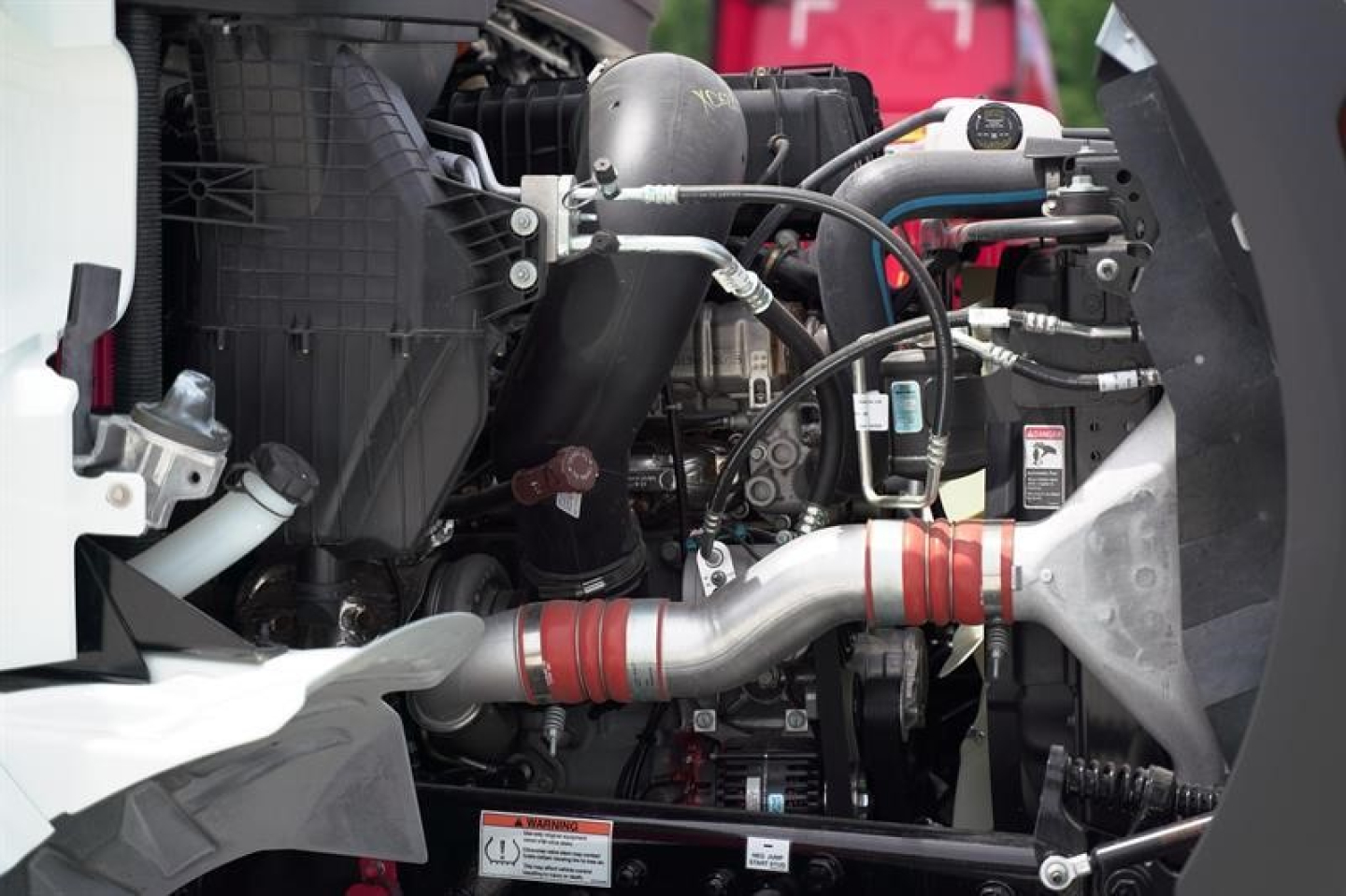 Engine bay of a 2027 Western Star 47X dump truck showing coolant hoses, metal piping, and engine components with labels and clamps.