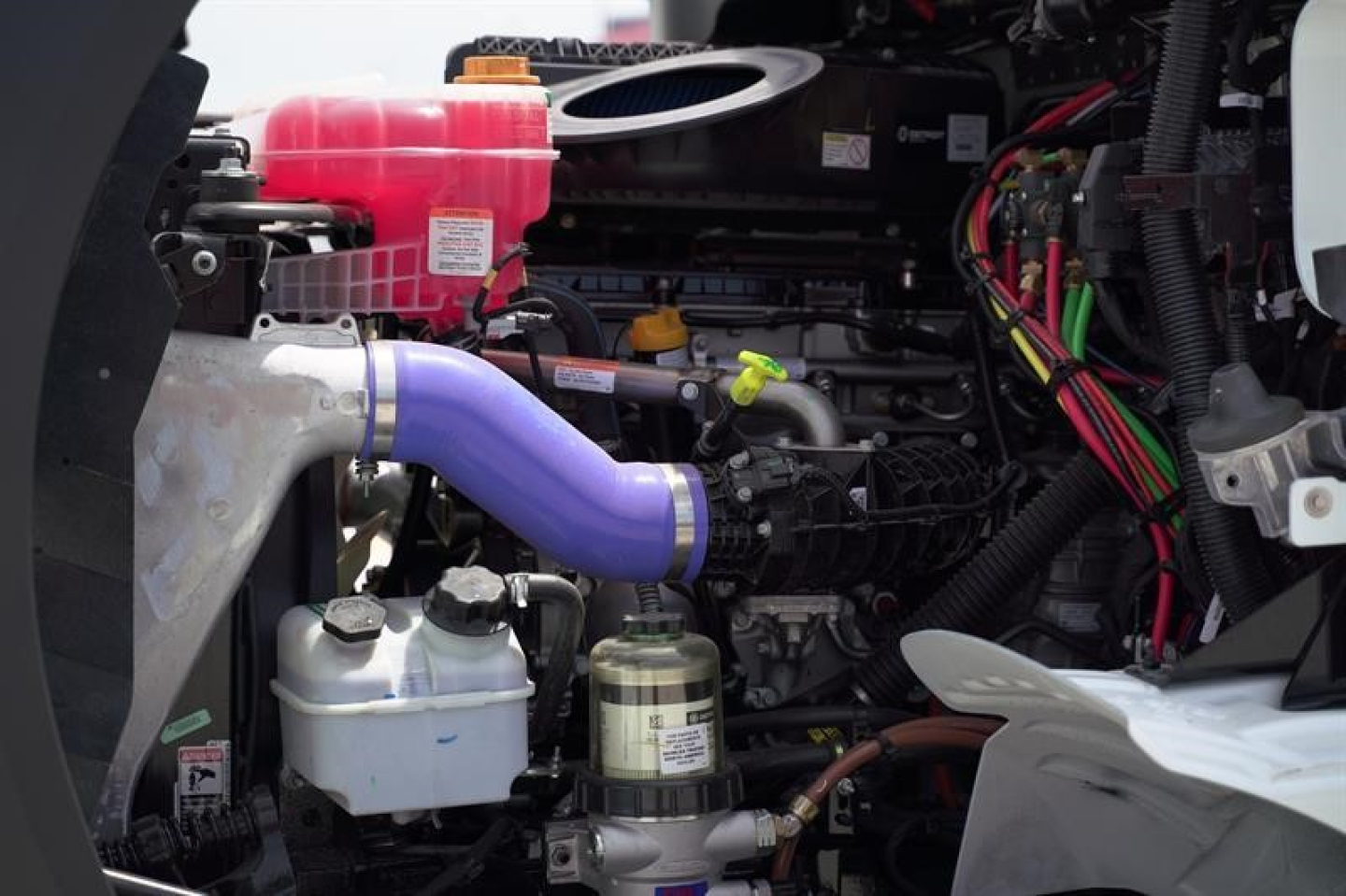 Engine bay of a Western Star 47X truck showing a pink coolant reservoir, purple hose, and various hoses and cables.