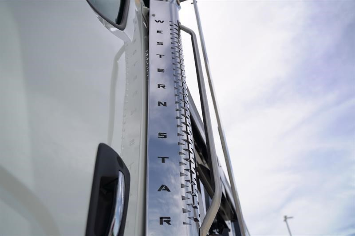 Western Star 47X truck side mirror area showing vertical chrome fuel/tank step with lettering, part of cab and sky background.