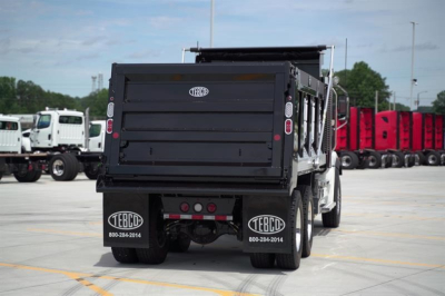 Dump truck bed rear view showing TECO or TEBC logo on mud flaps and back of cargo bed. Visible are taillights and hitch area.