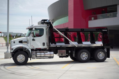 Western Star 47X dump truck in side profile view with white cab and chrome fuel tanks, black dump bed, parked near a modern building.