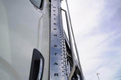 Western Star 47X truck side mirror area showing vertical chrome fuel/tank step with lettering, part of cab and sky background.