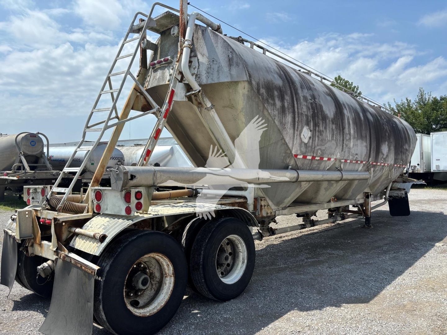 Pneumatic dry bulk trailer showing cylindrical stainless tank with rear stairs and dual rear axles.