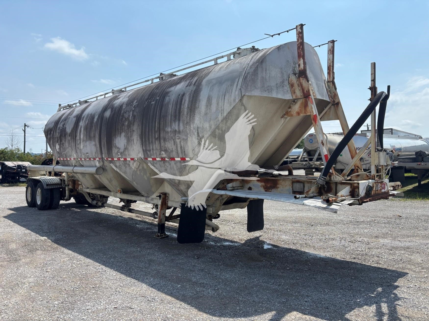 Pneumatic dry bulk trailer in in-service condition with weathered exterior and rear access chute showing rusted metal framework.
