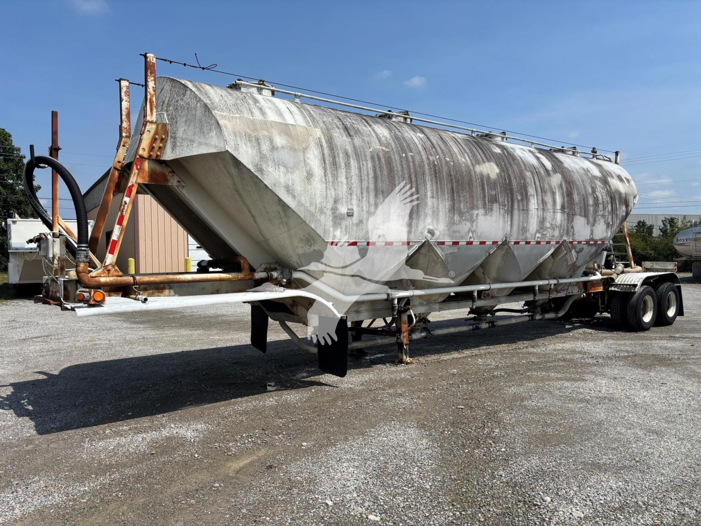 Trailer showing a Fruehauf pneumatic dry bulk tanker with a weathered aluminum tank, rear dual-axle and landing legs, various hoses and piping along top, and a hitch area.