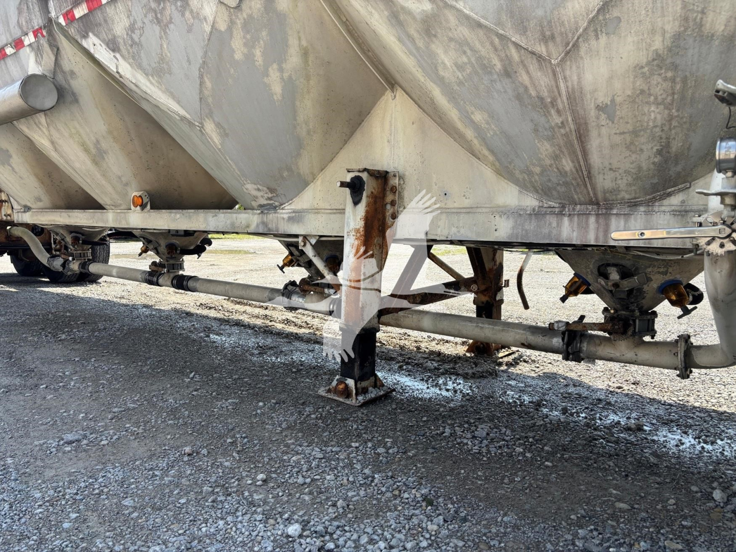 Pneumatic-dry bulk trailer undercarriage with landing legs and frame rails; weathered metal with rust spots and support beams visible.