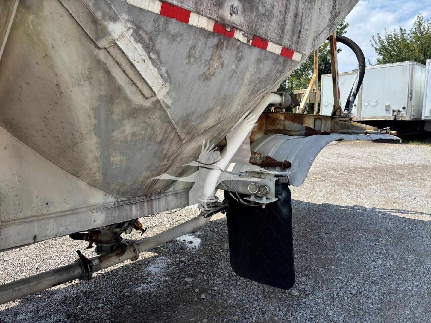 Trailer hitch and underside of a 1980 Fruehauf pneumatic dry bulk trailer showing unloading chute and mud flap with metal frame.