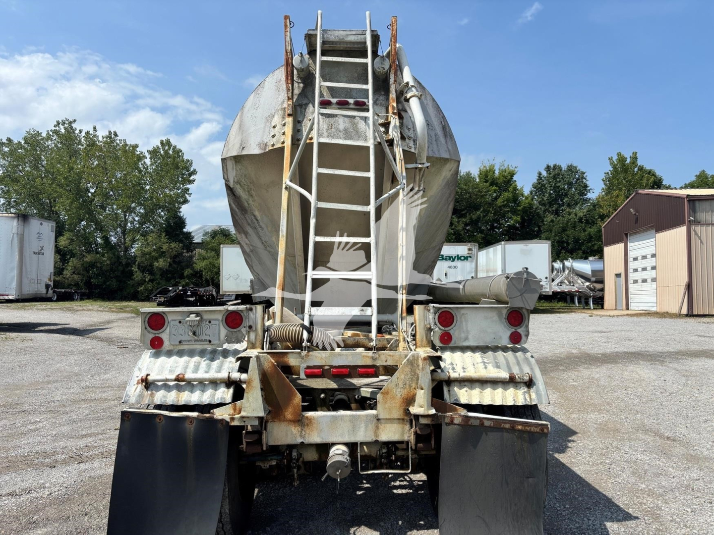 Rear view of a Fruehauf pneumatic dry bulk trailer with ladder and chute, showing weathered metal, dual landing gear, and rear bumper lights.