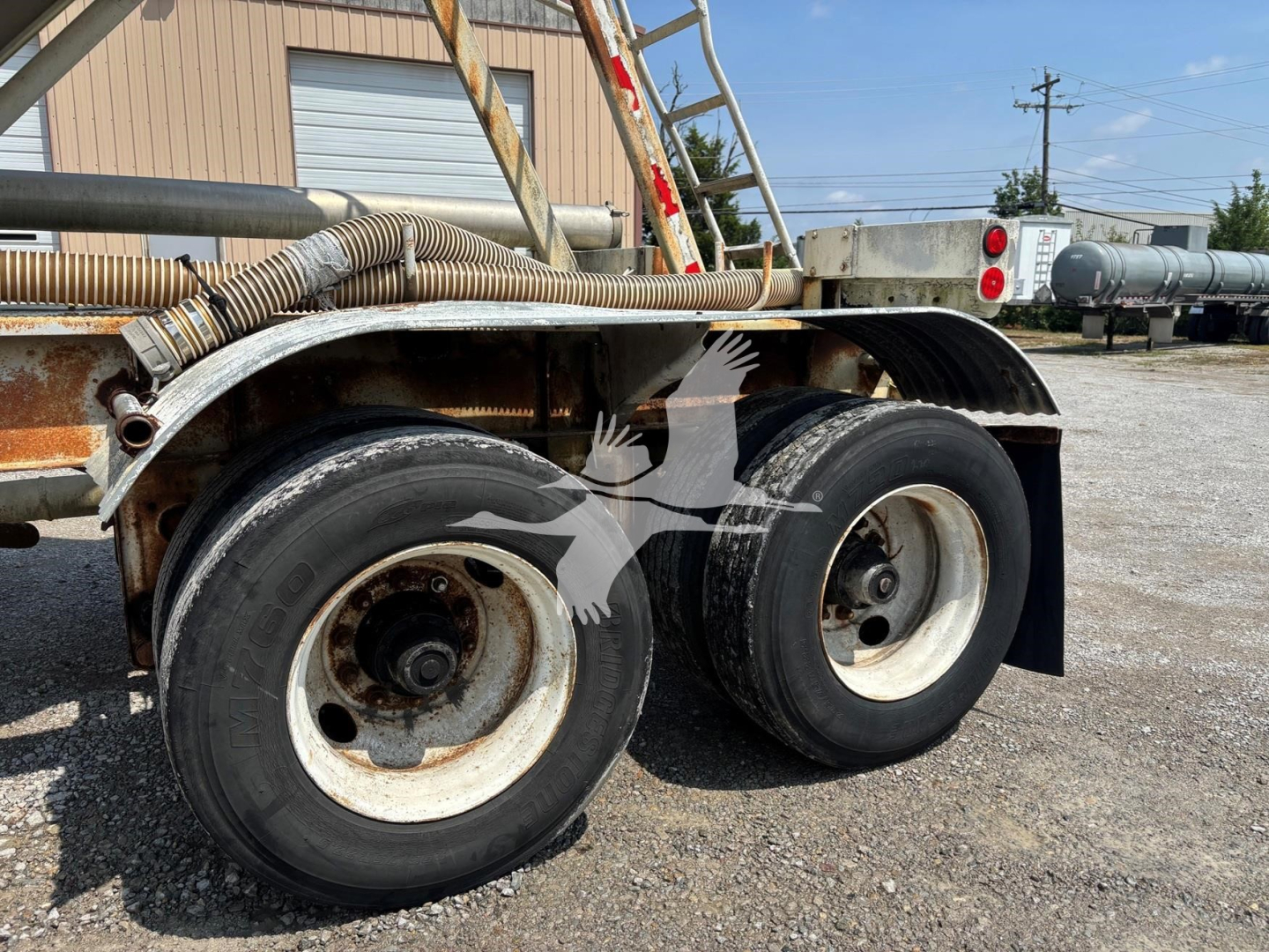 Fruehauf pneumatic dry bulk trailer axles and wheels with metal fenders and hoses, showing side view of dual tires and part of frame.