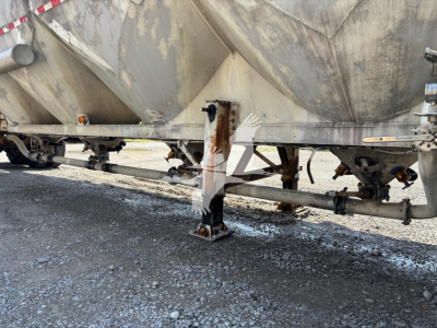 Pneumatic-dry bulk trailer undercarriage with landing legs and frame rails; weathered metal with rust spots and support beams visible.
