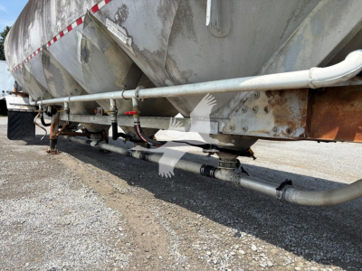 Fruehauf pneumatic dry bulk trailer undercarriage showing piping, hoses, and frame with rusted bracket along a gravel lot.