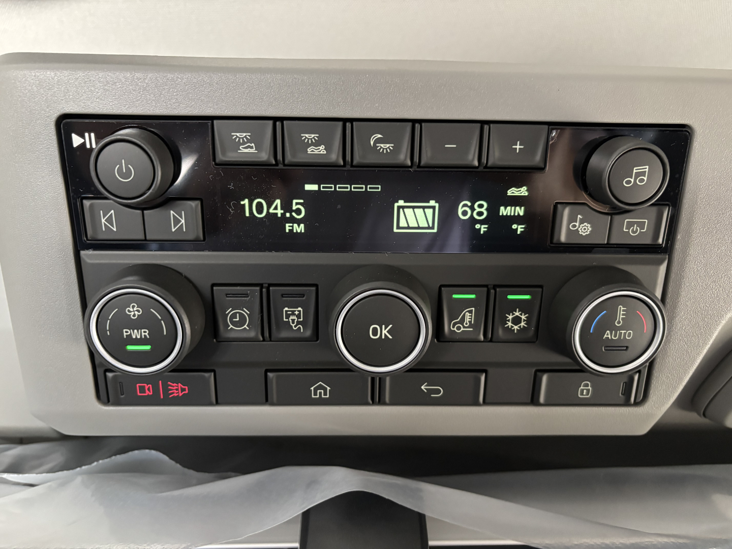 Truck cab radio and controls panel showing 104.5 FM, 68°F, settings buttons, OK button, and climate controls.
