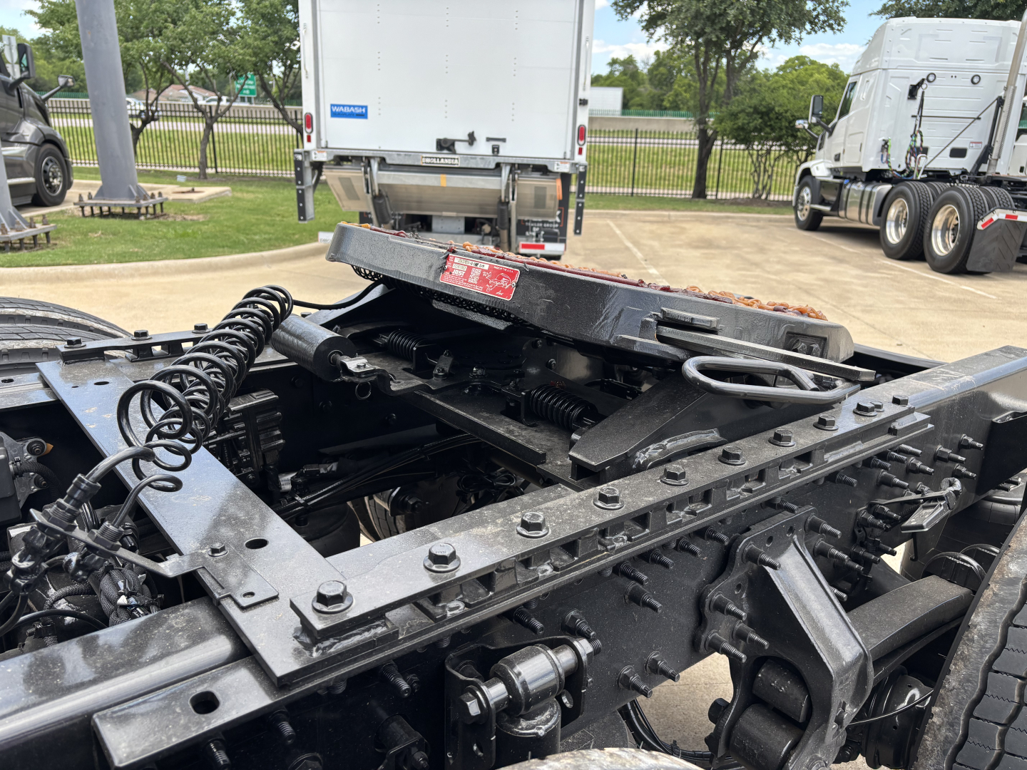 Truck chassis and fifth wheel area showing heavy-duty frame rails and slide rails with coiled air hoses and metal brackets.