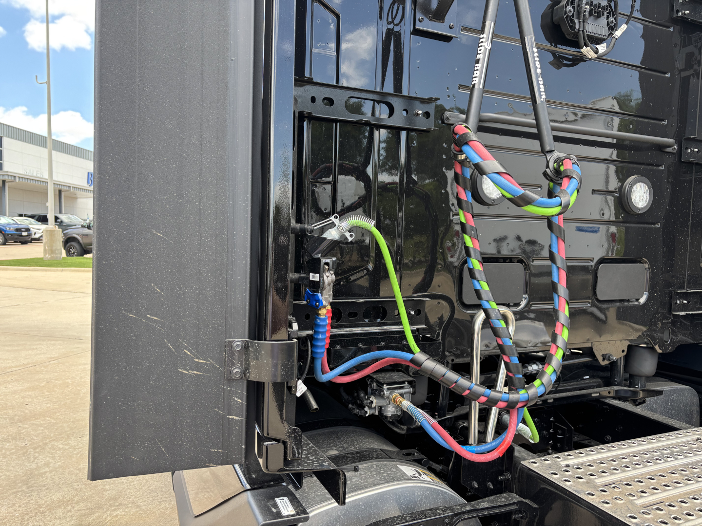 Trucks rear view showing wiring harnesses and connectors on a Volvo VNL tractor, with colorful braided cables and a metal frame nearby.