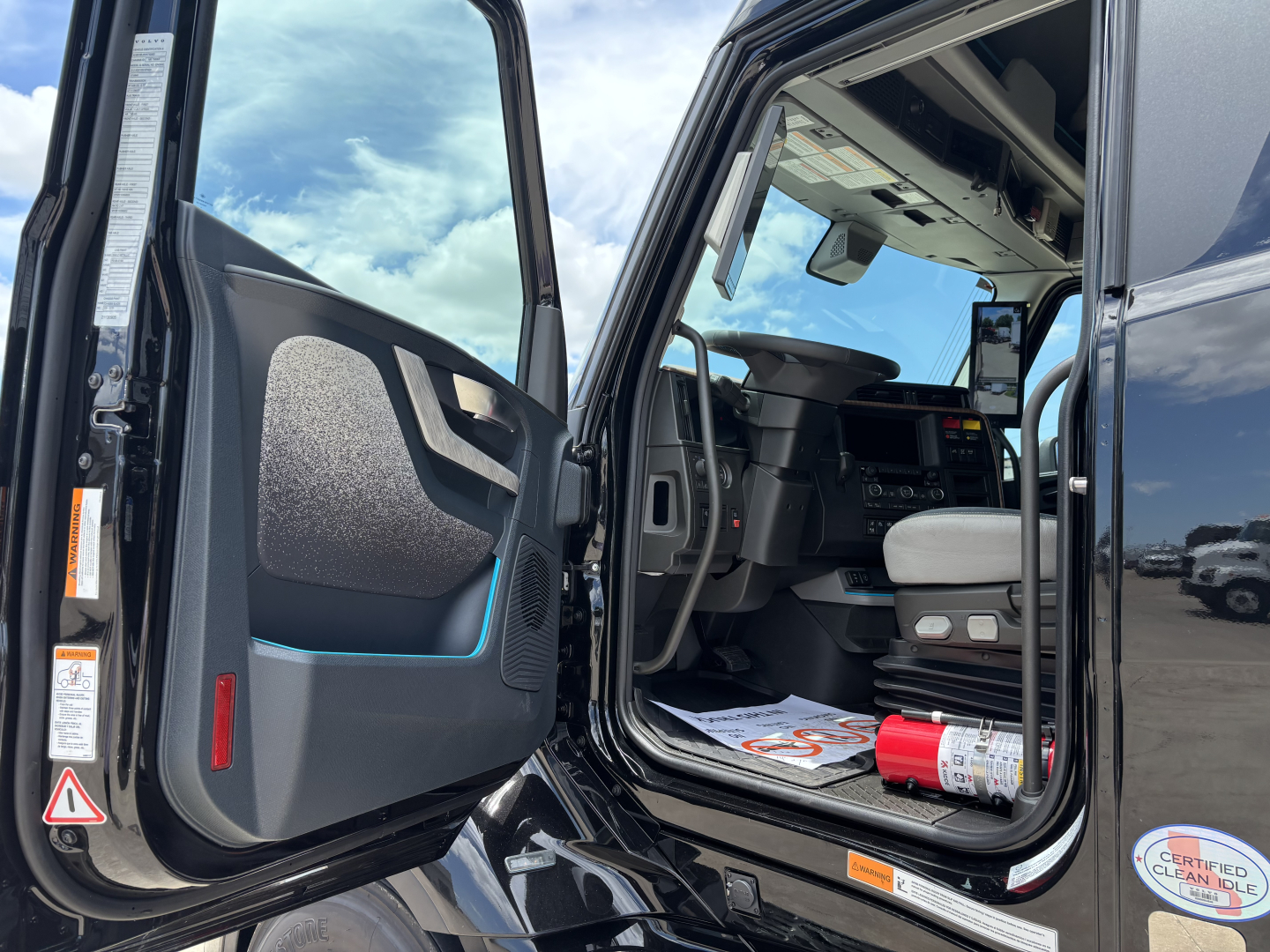 Truck cab interior of a 2027 Volvo VNL64T860 with driver's door open, visible dashboard, steering wheel, and seating area.
