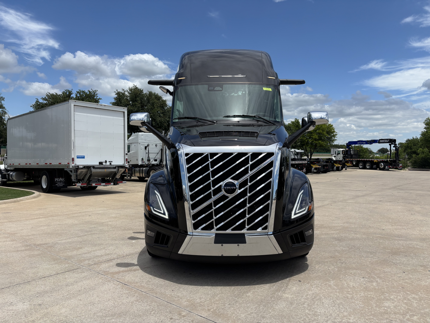 Front view of a blue 2027 Volvo VNL64T860 sleeper truck in a dealership lot, showing the distinctive chrome grille and Volvo emblem.