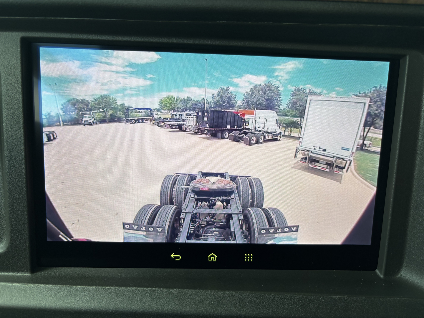 Volvo truck cab/drive line in view from interior camera showing rear dual-axle chassis and surrounding lot with trucks.