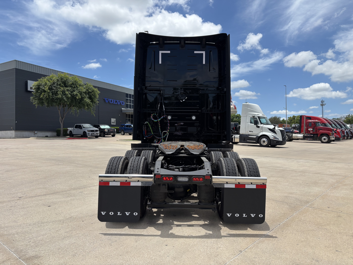 Volvo VNL64T860 tractor rear view showing fifth wheel, dual rear axles, and mud flaps with Volvo branding. Clear sky and dealership lot in background.