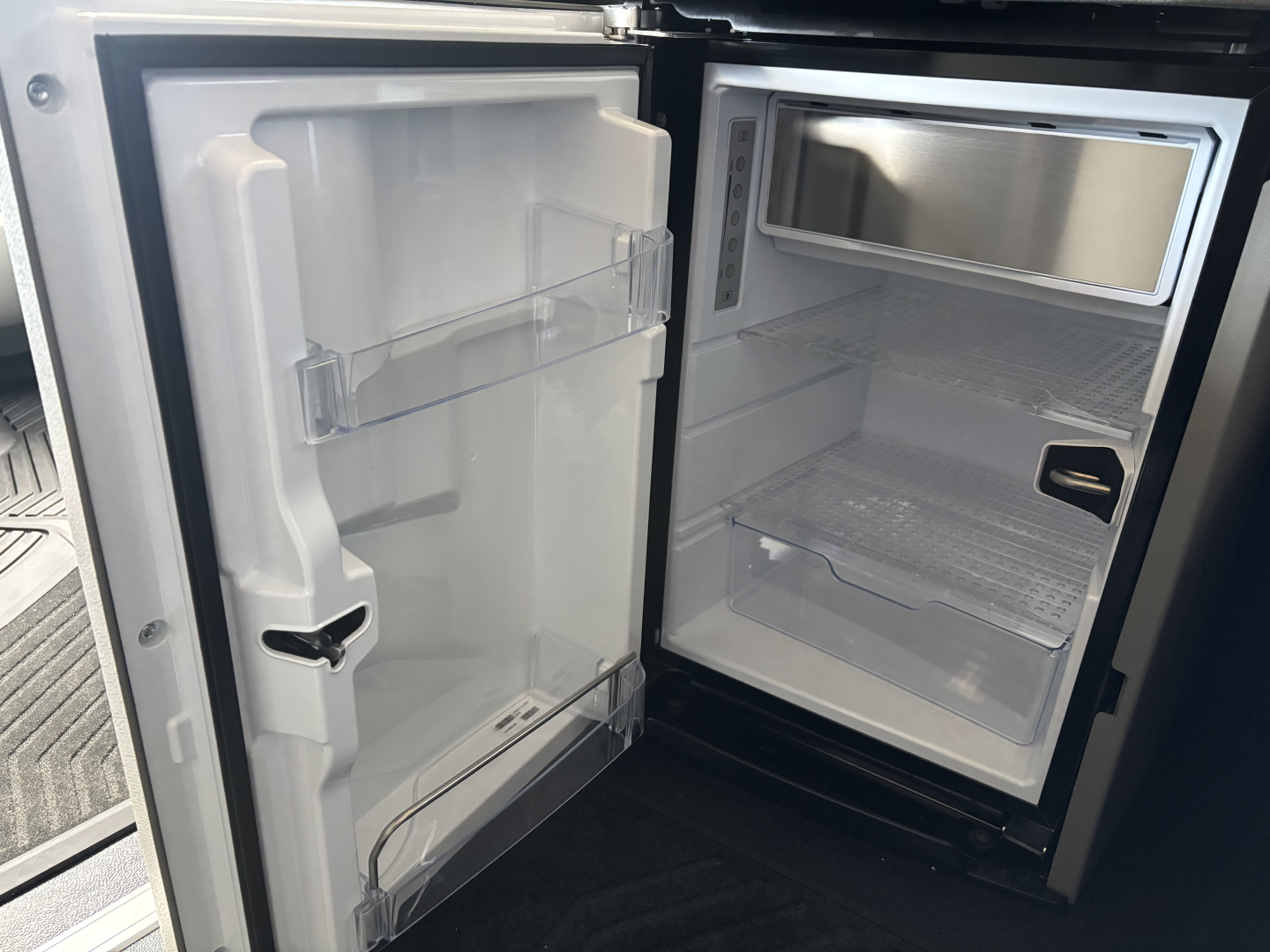 Volvo VNL64T860 cab refrigerator/freezer compartment open showing empty freezer and main refrigerator with shelves.