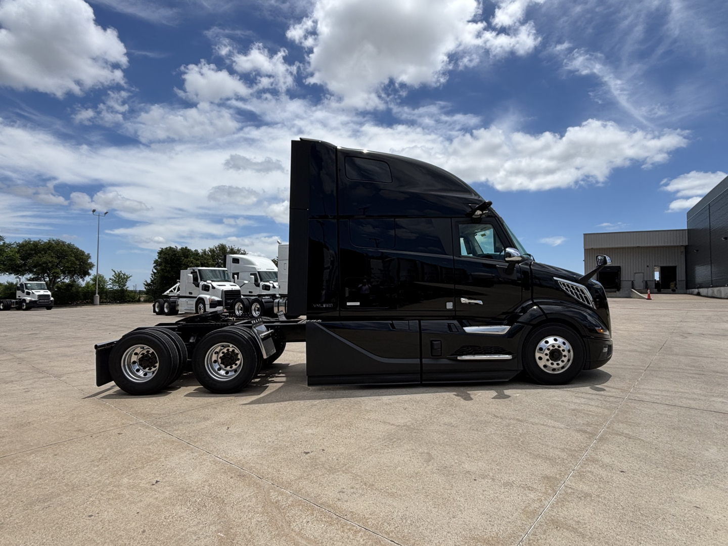 2027 Volvo VNL64T860 near-sleeper tractor in black, side view, showcased in lot with clear sky.
