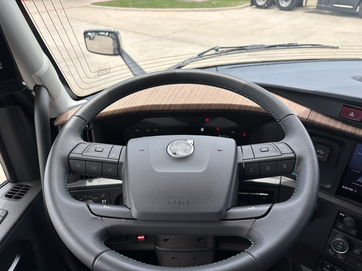 Volvo truck steering wheel view inside cab showing dashboard controls and wood trim.
