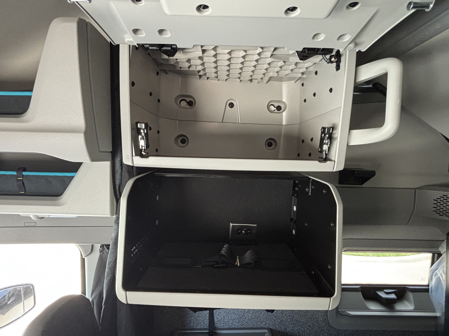 Volvo VNL64T860 sleeper cab storage compartments: upper small cubby with diamond pattern interior, lower open storage bin, side handle on right, interior metal panels.