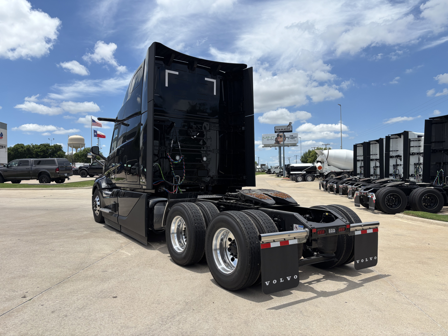 Truck cab with raised sleeper area, rear view showing tandem axles and electrical wiring panels in engine bay area; Volvo branding on mud flaps.
