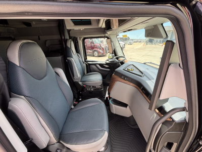 Volvo truck cab interior showing steering wheel, driver seat, and dashboard with light gray upholstery and wood trim.