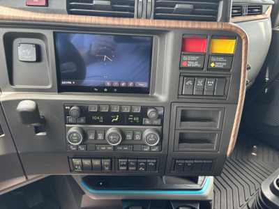 Truck dashboard panel showing navigation display, climate controls, and warning lights in a Volvo VNL cabin.