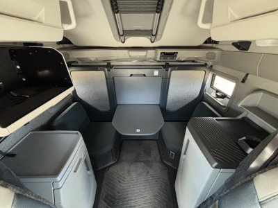 Interior view of a new 2027 Volvo VNL64T860 sleeper cab showing a compact lounge table, seating, and storage cabinets.
