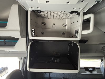 Volvo VNL64T860 sleeper cab storage compartments: upper small cubby with diamond pattern interior, lower open storage bin, side handle on right, interior metal panels.