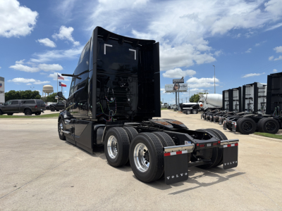 Truck cab with raised sleeper area, rear view showing tandem axles and electrical wiring panels in engine bay area; Volvo branding on mud flaps.