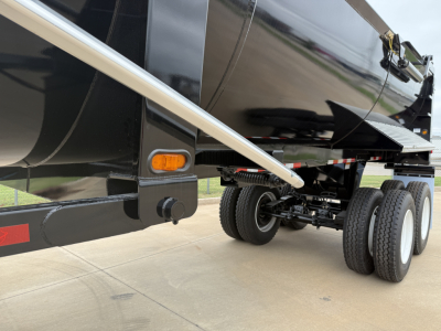 Trailer undercarriage showing tandem axles with dual tires and suspension from Armor Lite SHD32/48; side step/rail and orange side marker light visible.