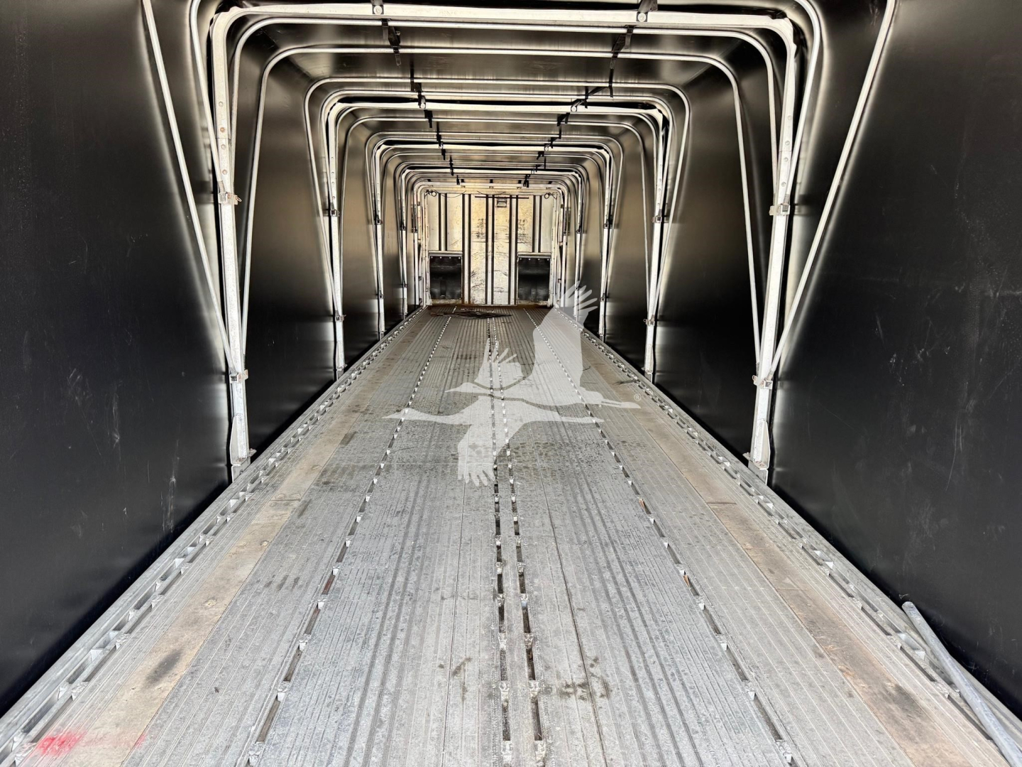 Trailer interior: aluminum curtain-side flatbed with ribbed metal floor and curved support frames forming a tunnel-like aisle.